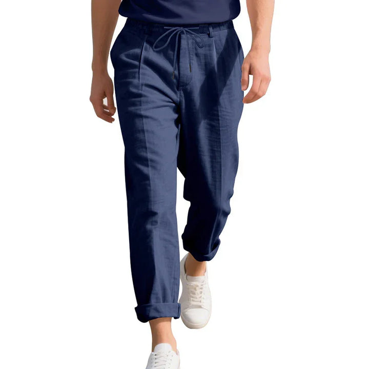 Man wearing navy blue drawstring pants with rolled cuffs and white sneakers on white background