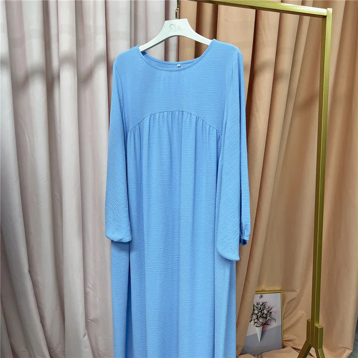 Light blue long-sleeve maxi dress on white hanger against beige curtains and gold clothing rack