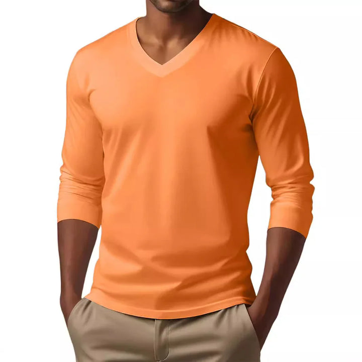 Man wearing bright orange V-neck long sleeve shirt with hands in beige pants pockets