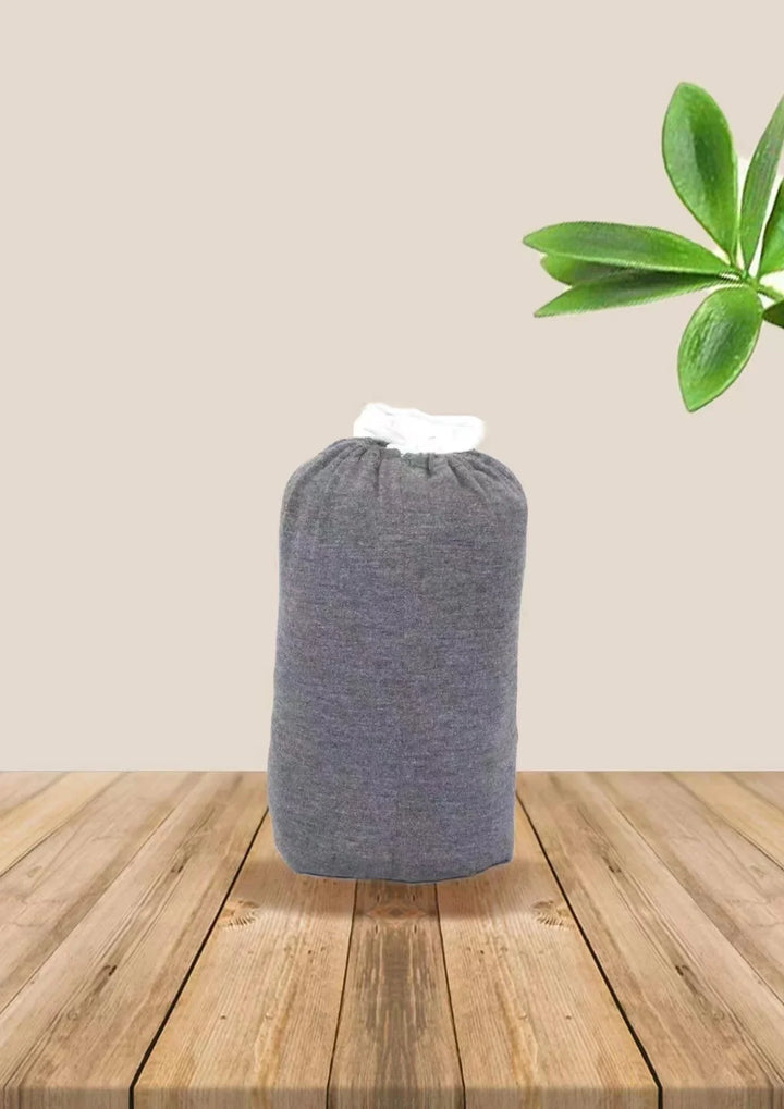 Gray fabric laundry bag with white drawstring on wooden surface with green plant leaves