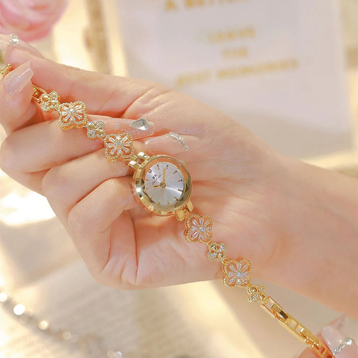 Elegant gold bracelet watch with floral design and jeweled accents held in hand with manicured nails
