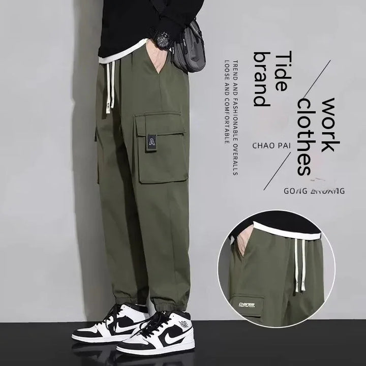 Men's olive green cargo pants with large pockets and drawstring waist, paired with black and white sneakers
