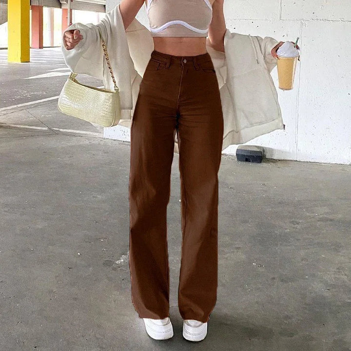 Woman wearing brown wide-leg pants, white crop top, white jacket, white sneakers, holding beige handbag and iced coffee in parking garage