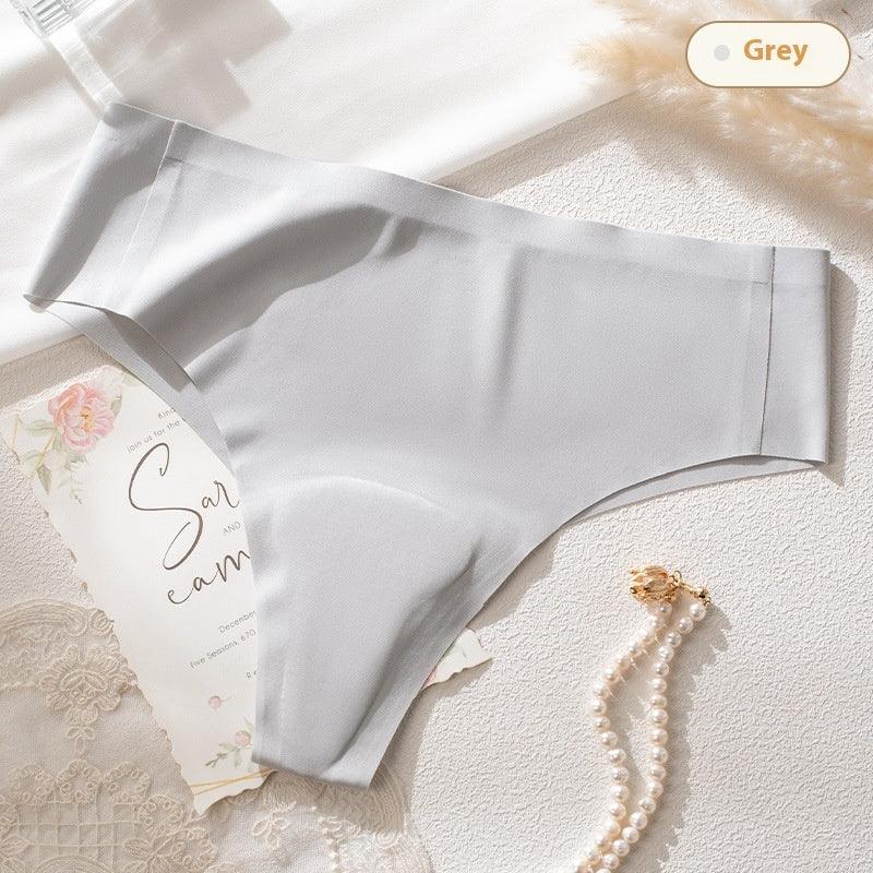 Grey seamless women's underwear thong on textured surface with pearl necklace and floral card