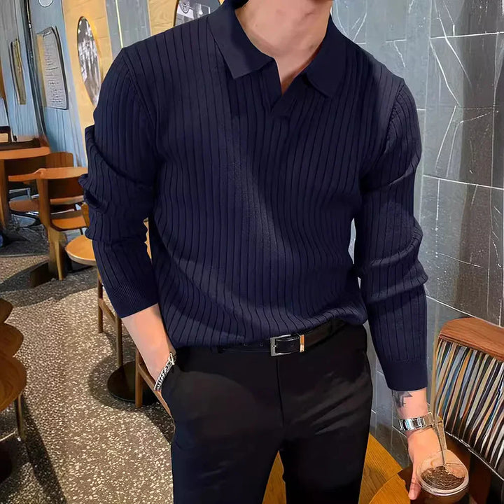 Man in navy ribbed knit polo sweater and black pants holding iced coffee in modern cafe
