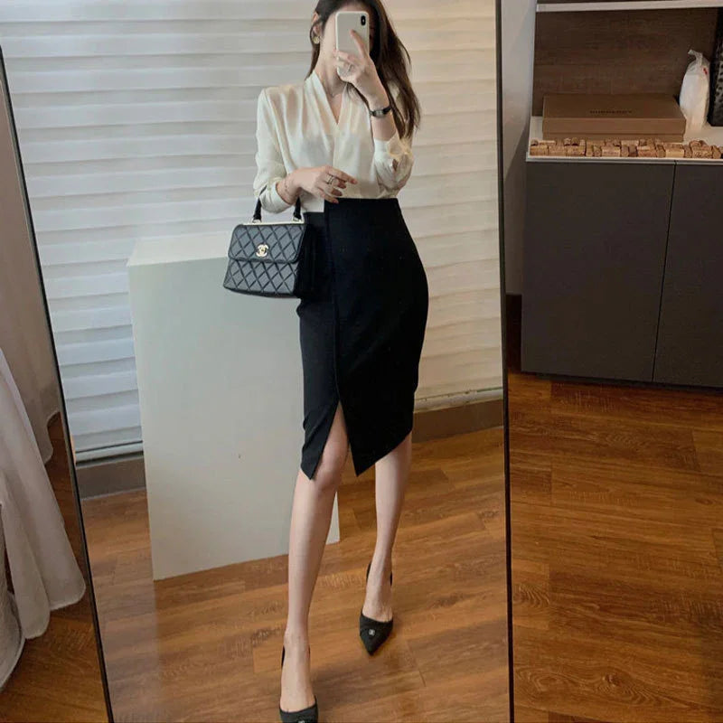 Woman in white blouse and black pencil skirt with slit, holding black quilted handbag, wearing black heels