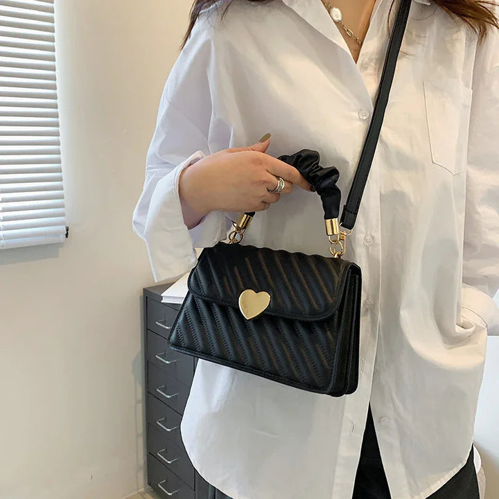 Woman in white shirt holding black quilted handbag with gold heart clasp and scrunchie handle