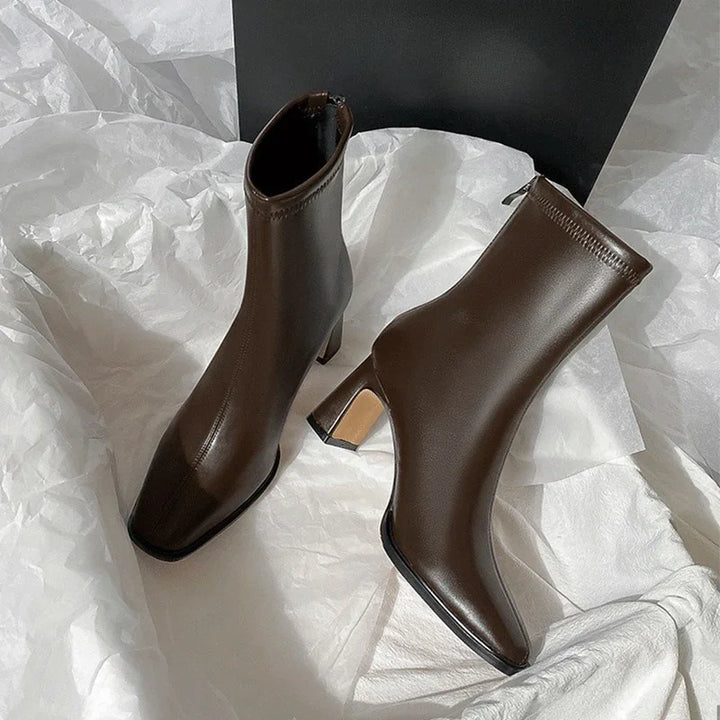 Pair of stylish dark brown leather ankle boots with block heels on white crumpled paper