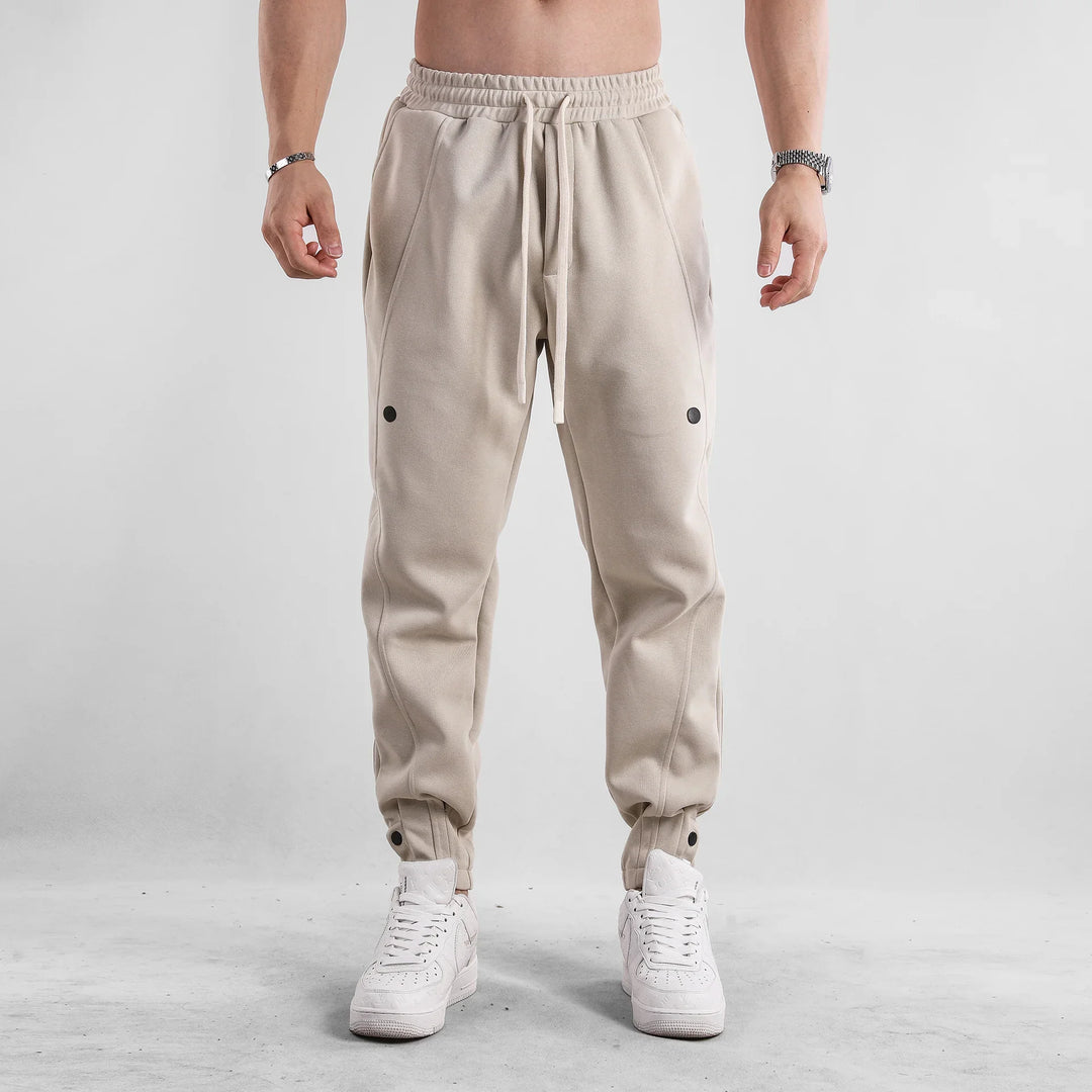 Man wearing beige jogger pants with black dots and white sneakers against gray background