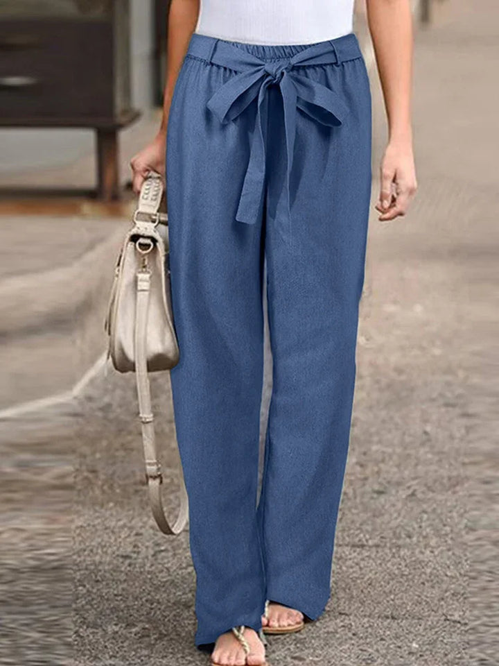 Woman wearing casual blue wide-leg pants with a tied waist belt, carrying beige handbag
