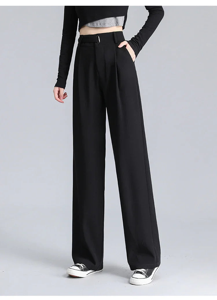 Woman wearing high-waisted black wide-leg pants with belt detail and black sneakers