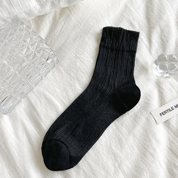 Black ribbed ankle sock displayed flat on white fabric with clear textured glass decorative items