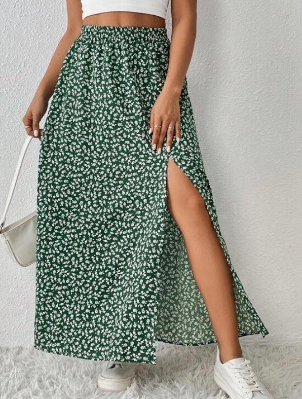 Woman wearing green floral maxi skirt with side slit, white crop top, white sneakers, and white handbag