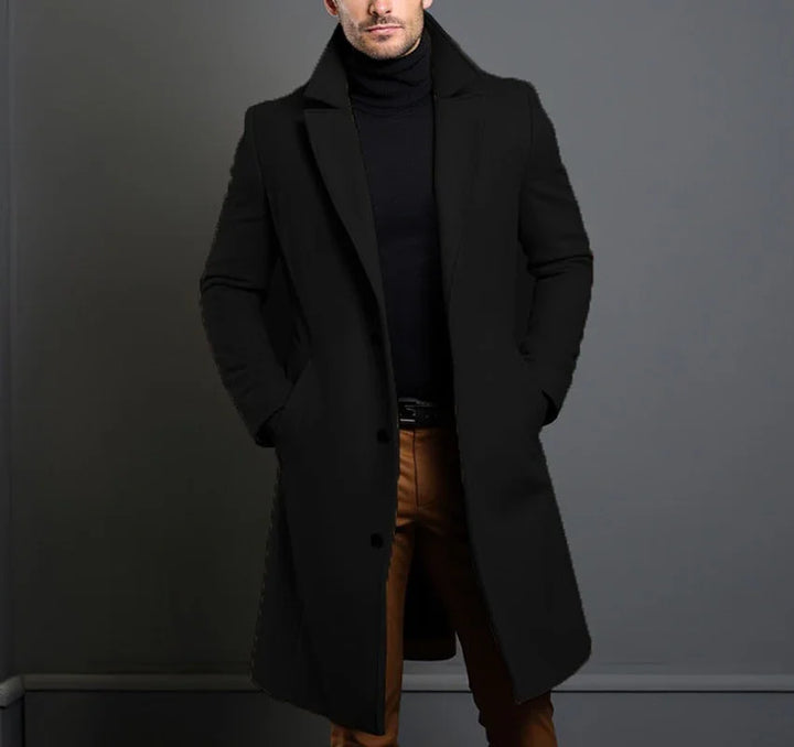 Man wearing stylish black overcoat and black turtleneck with brown pants against gray background