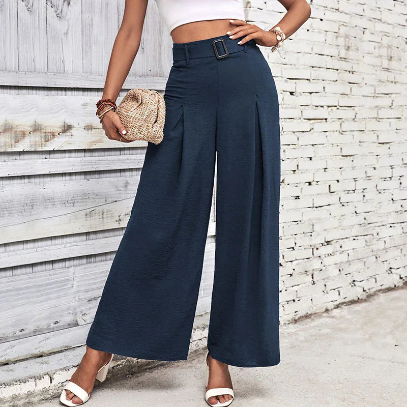 Woman wearing high-waisted navy wide-leg pants with belt and white crop top, holding woven clutch
