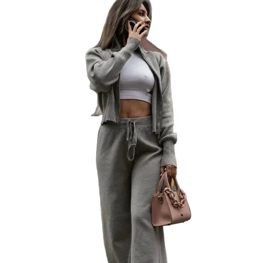 woman in gray casual loungewear set with cropped jacket and pants holding pink handbag, talking on phone