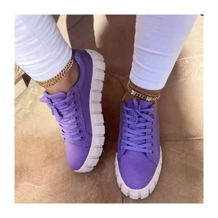 Purple casual sneakers with thick white soles worn with white pants and gold anklets on tile floor
