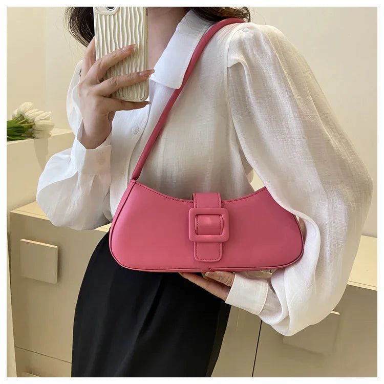 Woman wearing white blouse and black skirt holding pink shoulder bag with square buckle