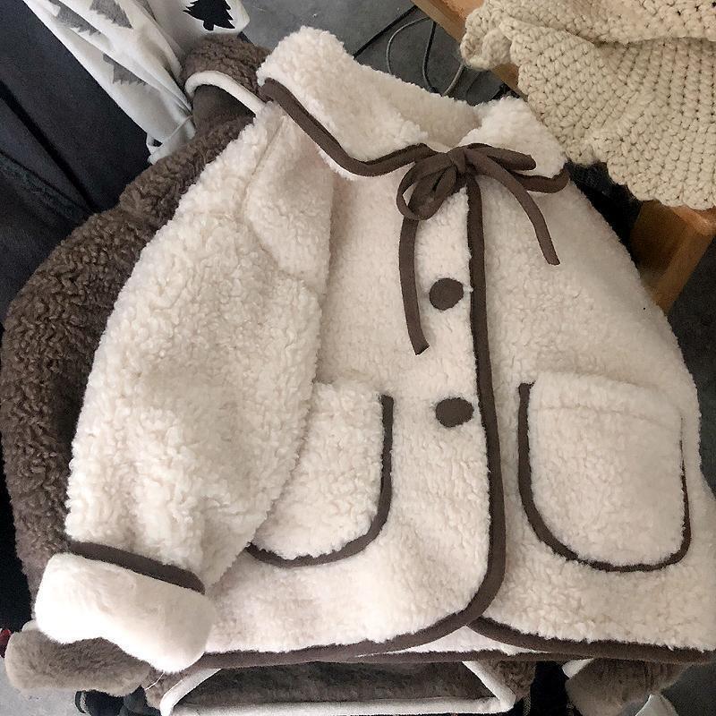 White sherpa fleece jacket with brown trim, buttons, and bow tie detail on a wooden chair