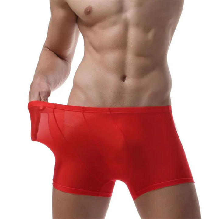 Muscular male torso wearing and stretching red sheer boxer briefs on white background