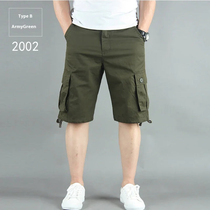 Man wearing army green cargo shorts with pockets, white sneakers, and a white shirt on gray background