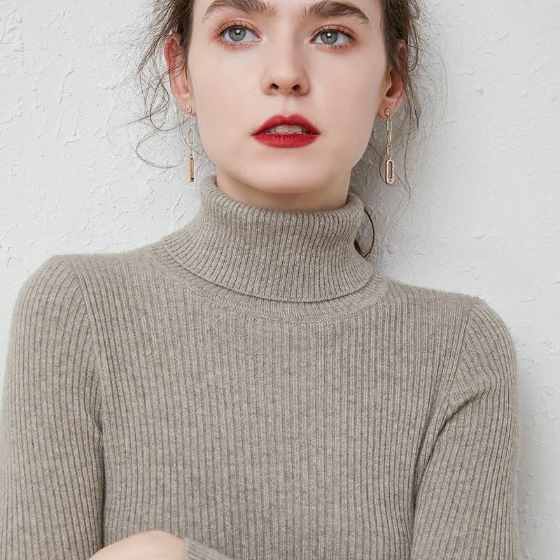 Close-up of woman wearing a beige ribbed turtleneck sweater with gold chain earrings and red lipstick