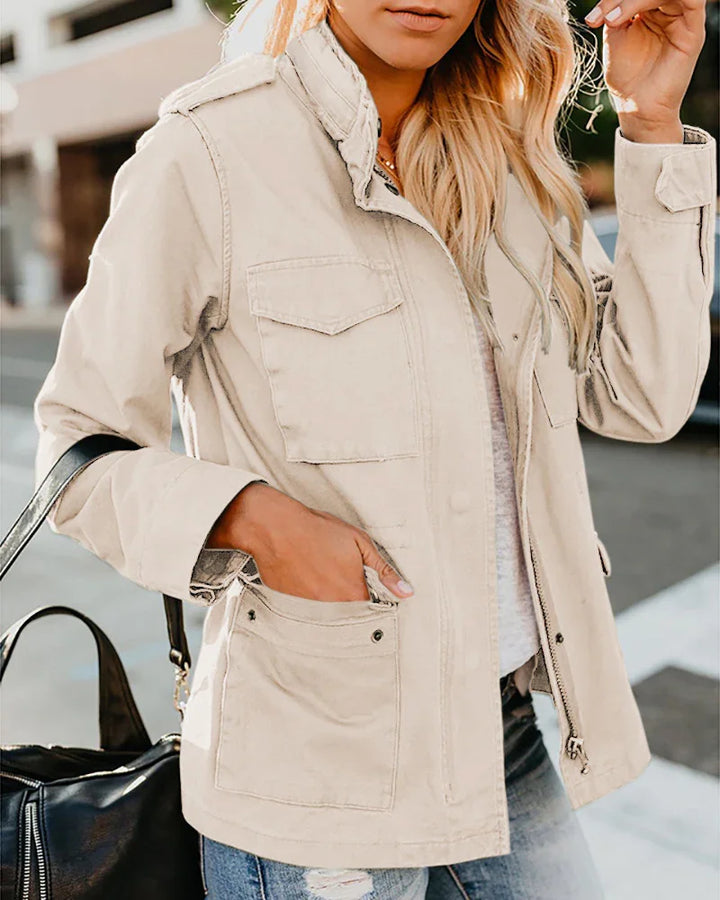 Woman wearing a beige utility jacket with front pockets, white top, ripped jeans, and carrying a black leather bag
