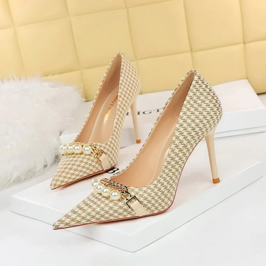 Beige houndstooth high heel pumps with pearl and chain embellishments on white box