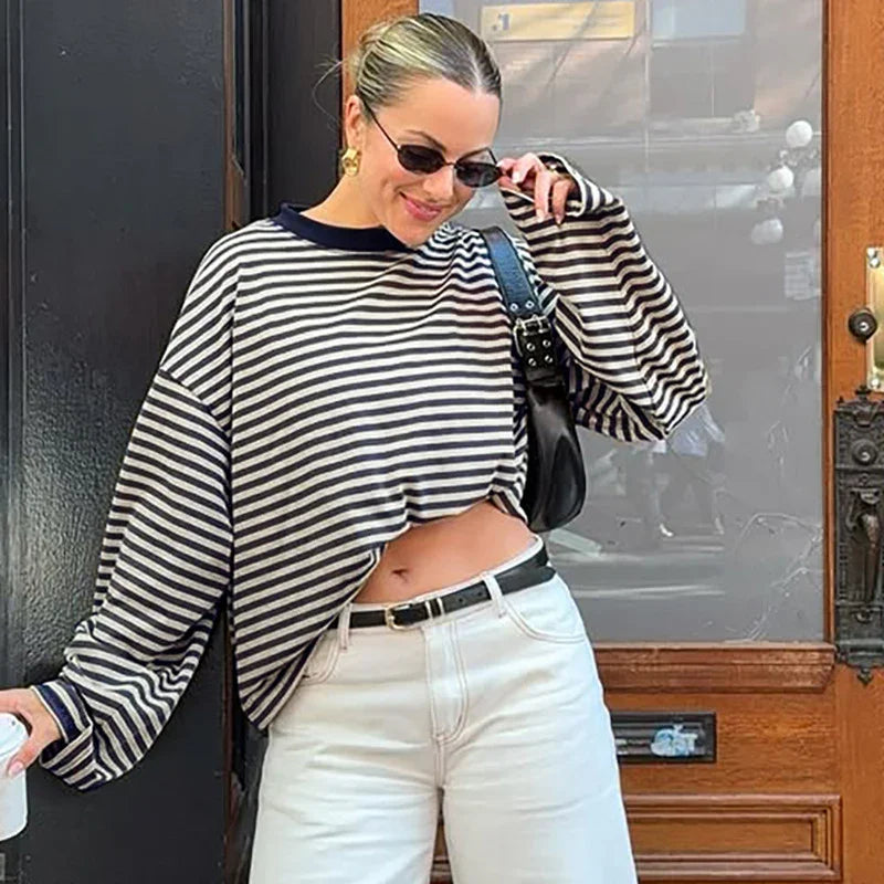Woman wearing black and white striped cropped sweater, white pants, sunglasses, carrying black handbag