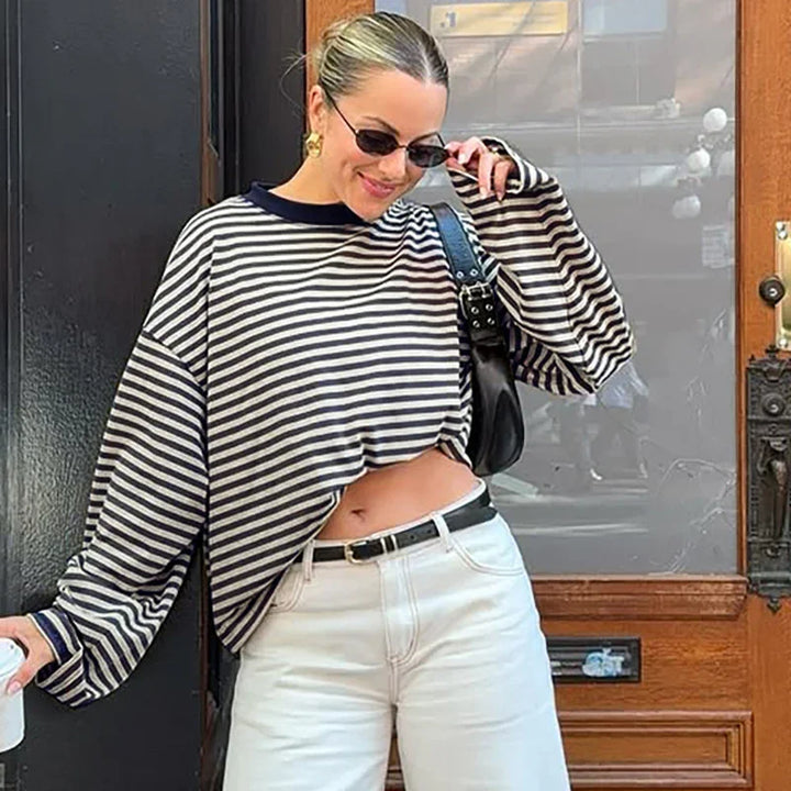 Woman wearing black and white striped cropped sweater, white pants, sunglasses, carrying black handbag