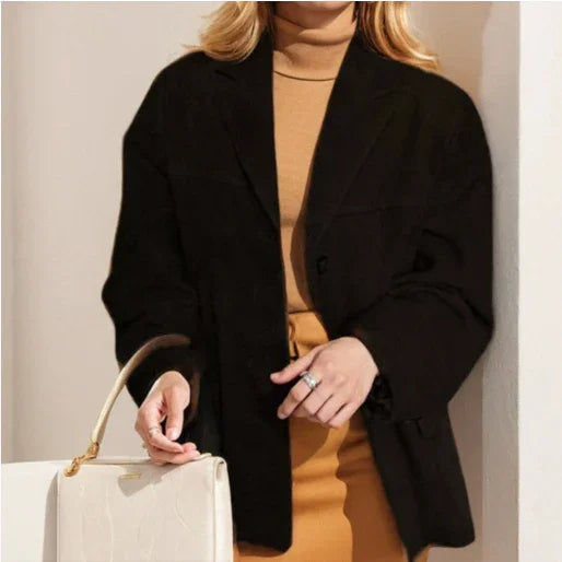 Woman wearing black blazer and camel turtleneck dress holding white handbag