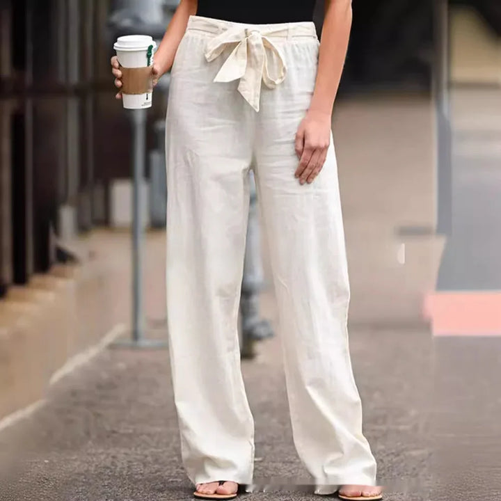 Woman wearing high-waisted white linen pants with a tied waistband holding a coffee cup