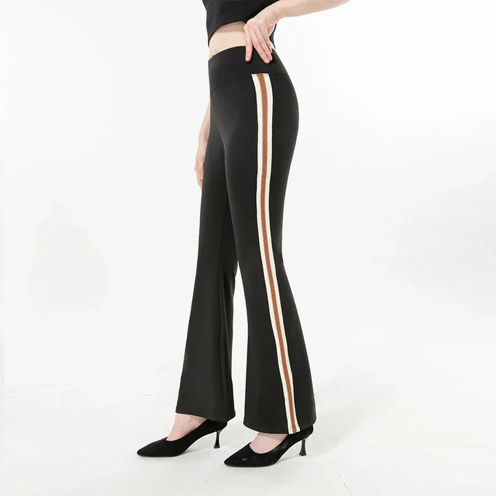 Black flare pants with white and brown side stripes worn with black heels on white background