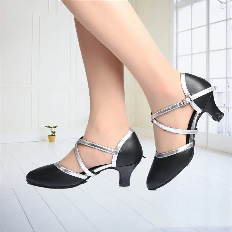 Black and silver women's dance heels with ankle straps on white floor by window