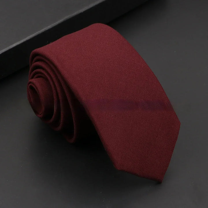 Rolled-up burgundy red necktie on a black surface with a black box in the background