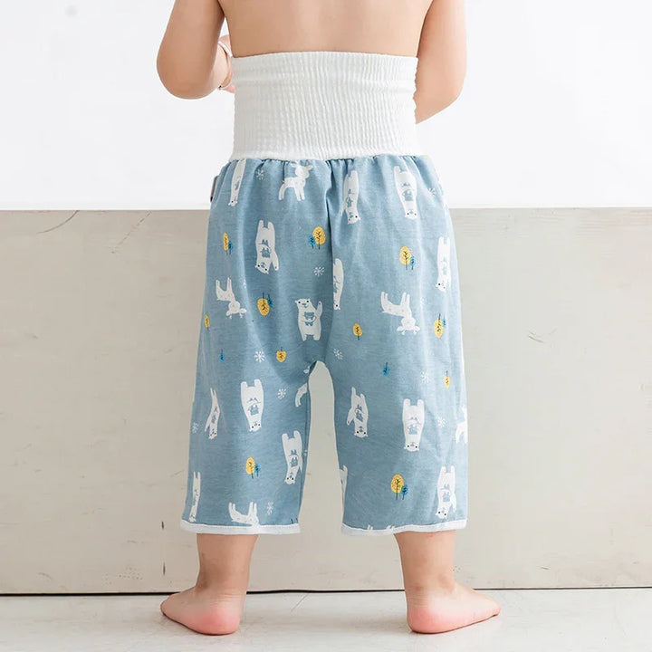 Toddler wearing blue pants with white bear and tree prints, standing barefoot on floor
