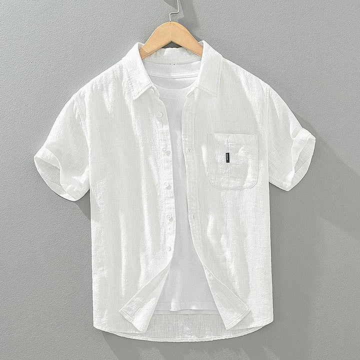 White short-sleeve button-up shirt with front pocket over white T-shirt on wooden hanger