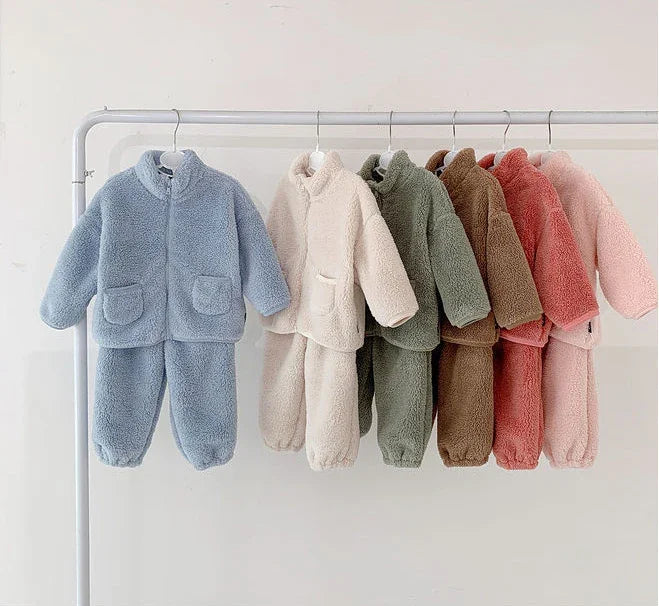 Cozy fleece baby clothing sets in blue, cream, green, brown, red, and pink hanging on a white rack
