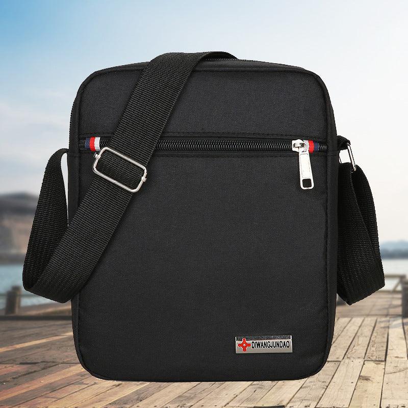 Black crossbody shoulder bag with adjustable strap and front zipper pocket, outdoor wooden pier background