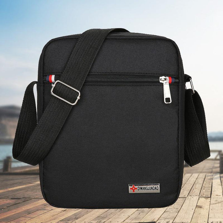 Black crossbody shoulder bag with adjustable strap and front zipper pocket, outdoor wooden pier background