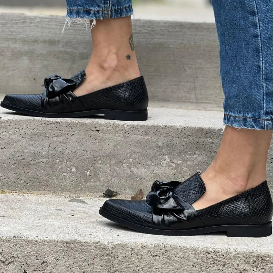 Black textured leather loafers with large bow detail worn with blue frayed hem jeans on concrete steps