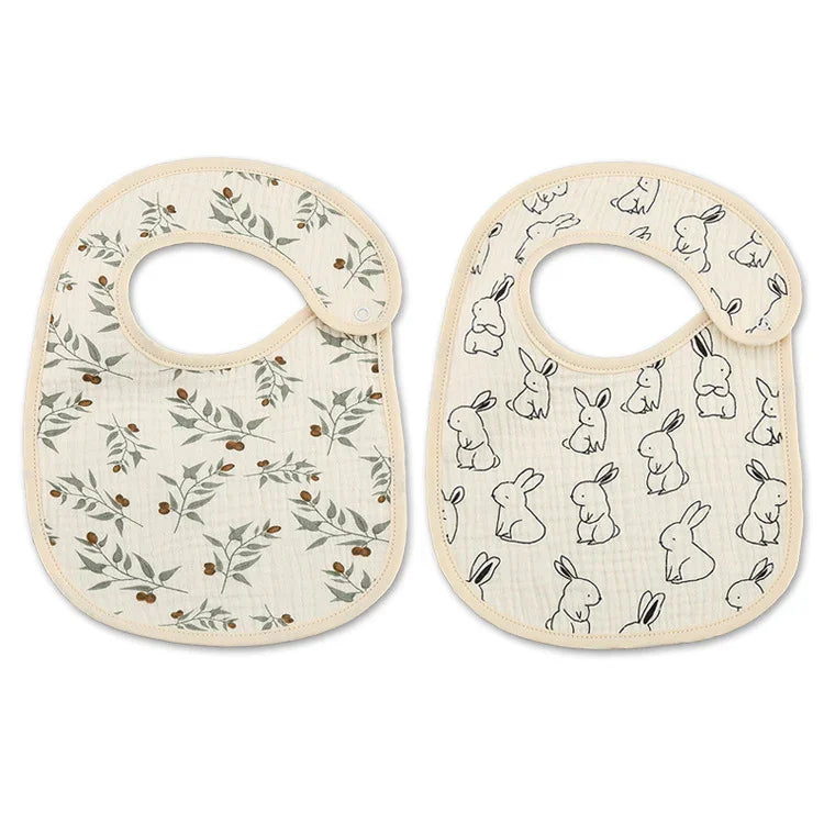 Two soft cotton baby bibs with beige trim, one with olive branch print, one with black bunny illustrations