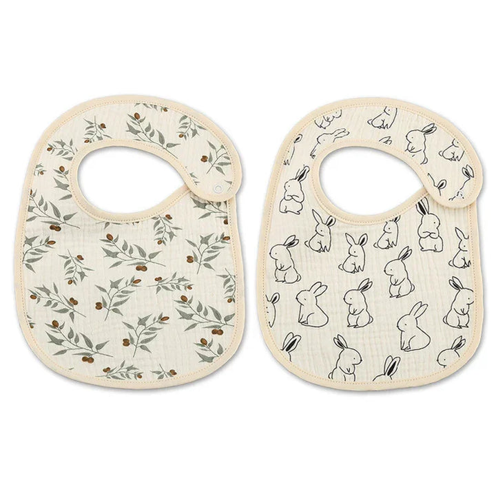 Two soft cotton baby bibs with beige trim, one with olive branch print, one with black bunny illustrations