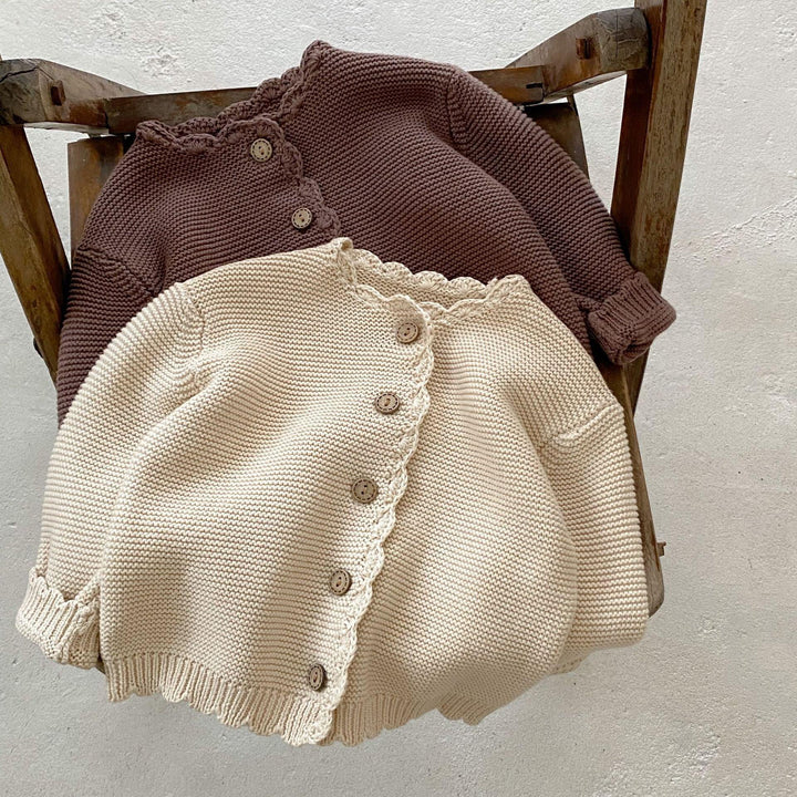 Two knitted baby cardigans in cream and brown with wooden buttons on rustic wooden chair
