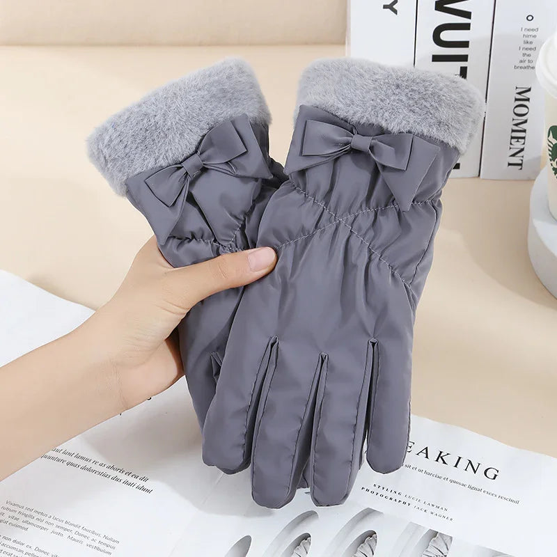 Pair of gray winter gloves with faux fur cuffs and decorative bows held by a hand over a magazine