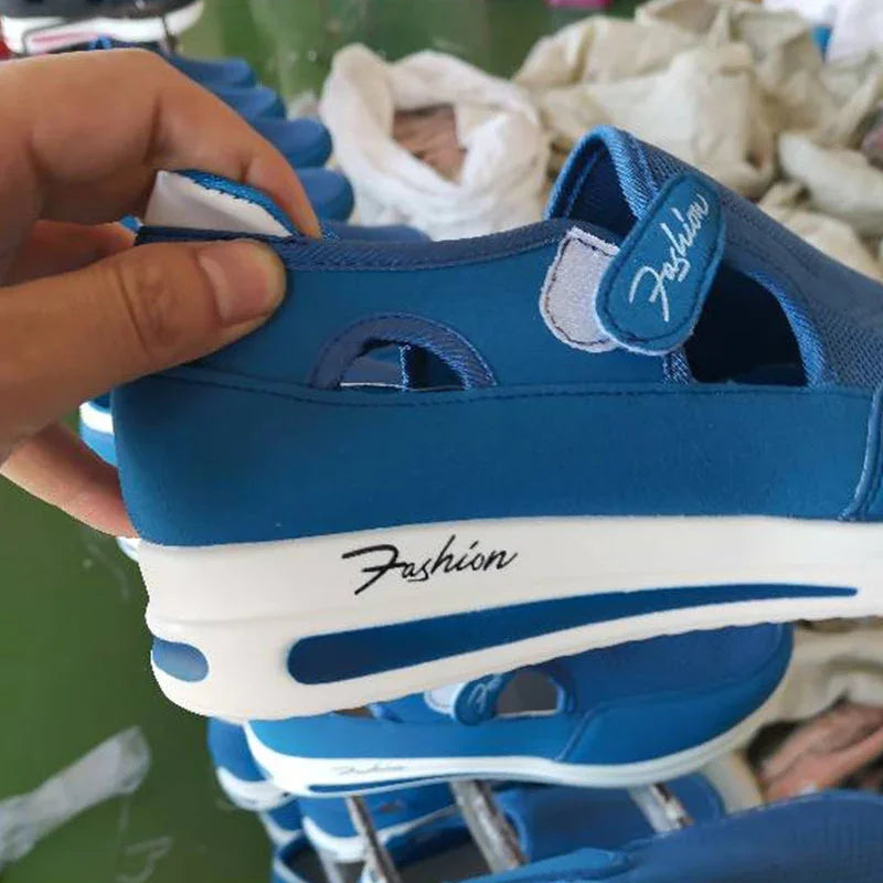 Hand holding blue casual sneaker with white sole and 'Fashion' text on side in factory setting