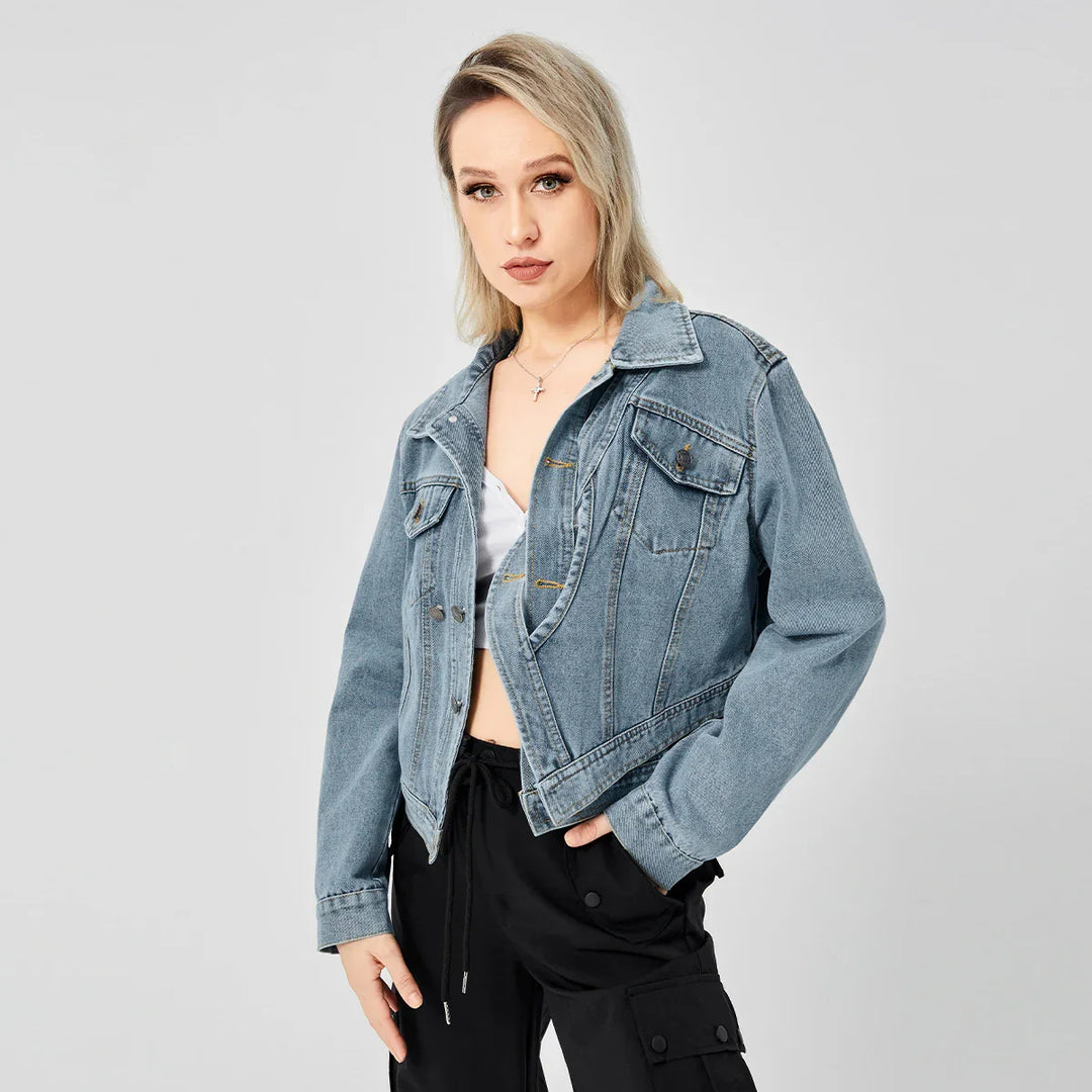 Blonde woman wearing light blue denim jacket over a white crop top and black cargo pants on gray background