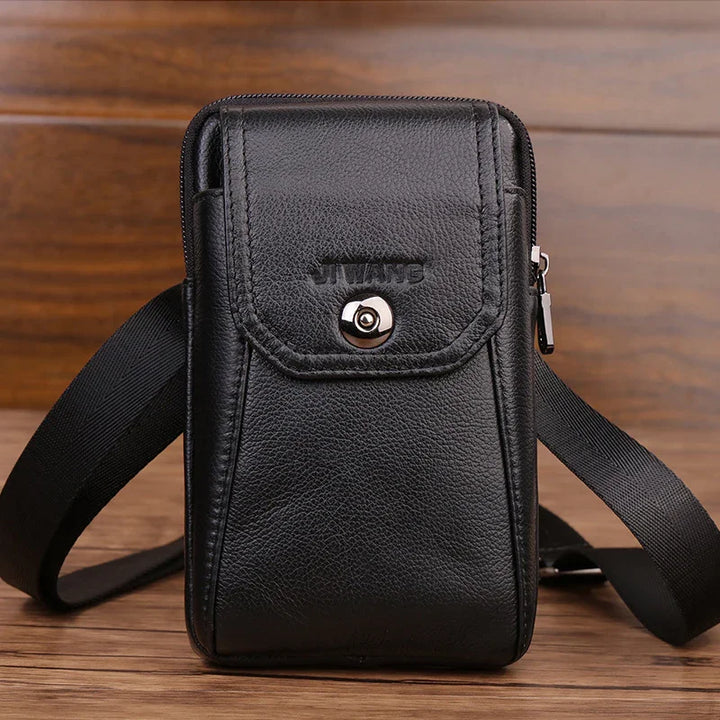 Black leather crossbody bag with front flap pocket and silver button on wooden surface
