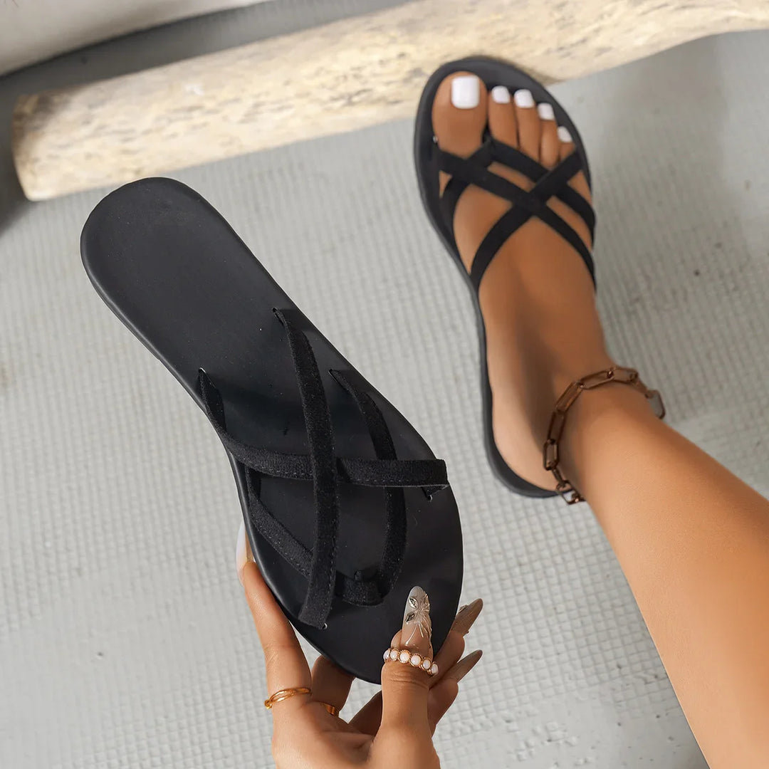 Black strappy flat sandals on feet and in hand with white nail polish and ankle bracelet