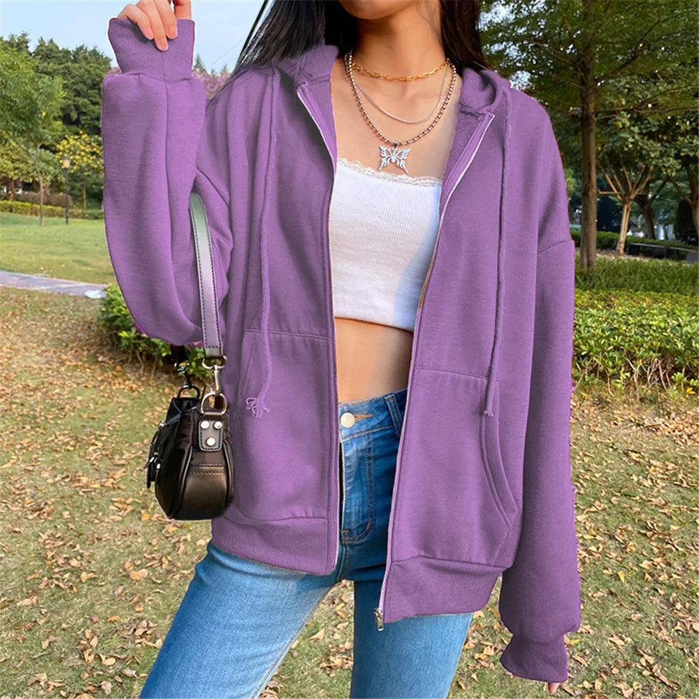 Woman wearing oversized purple zip-up hoodie, white crop top, blue jeans, and carrying black handbag outdoors